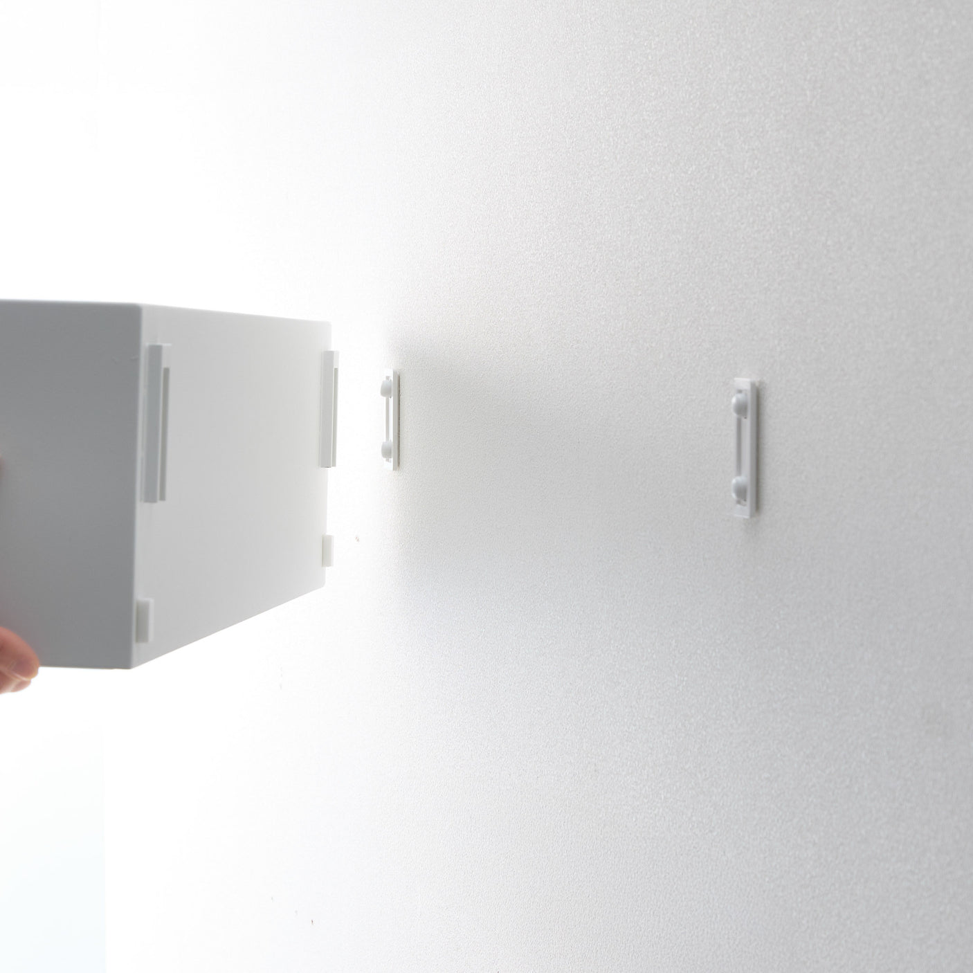 Person fester hvit oppbevaringsboks på vegg.