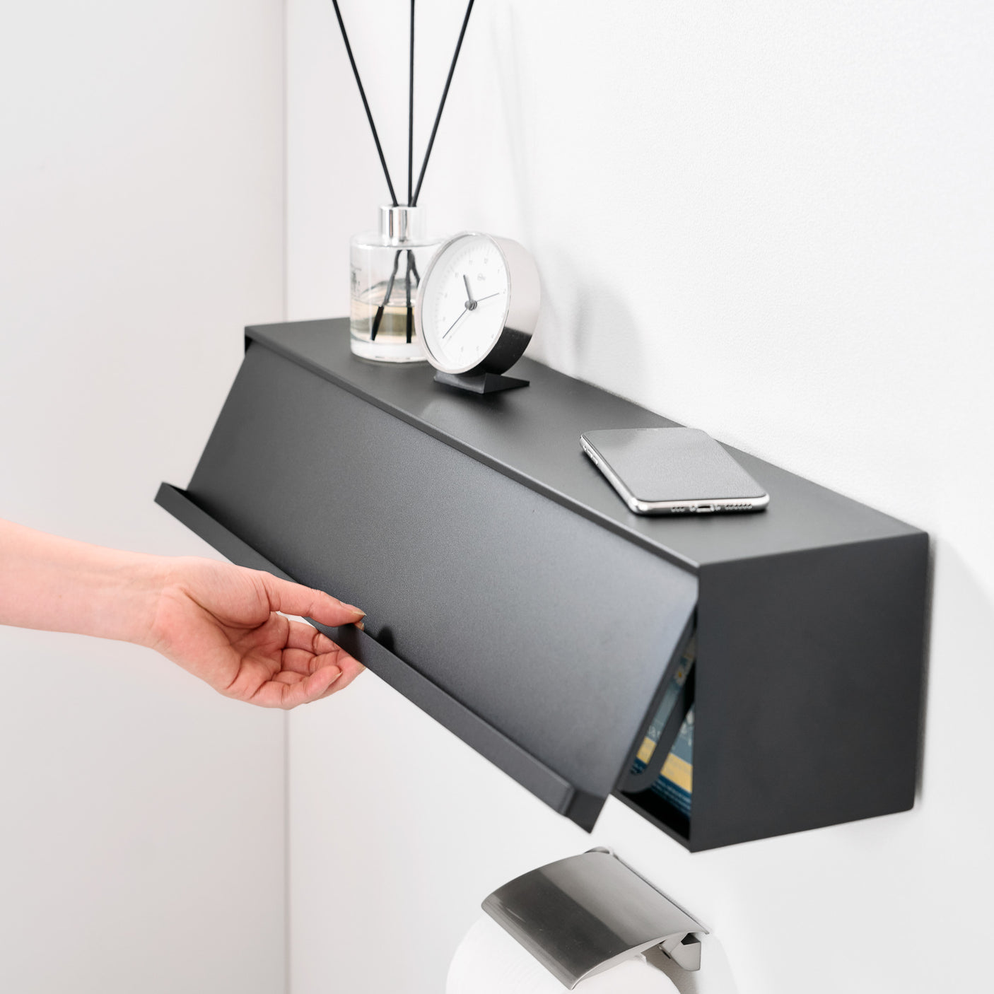 Sort veggboks i metall montert på vegg med duftpinner og klokke.