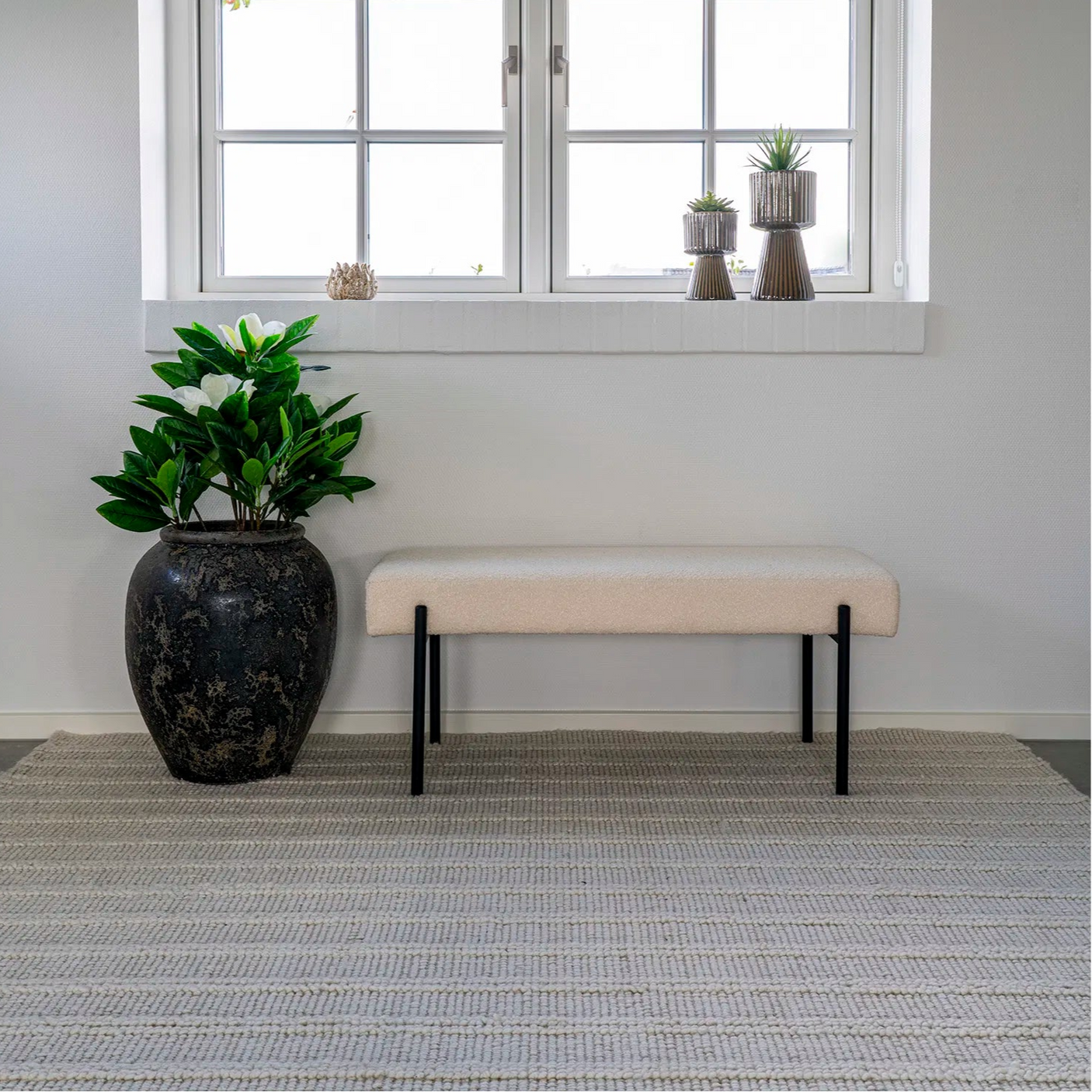 House Nordic bouclébenk med sorte metallben plassert foran et vindu i et lyst interiør.