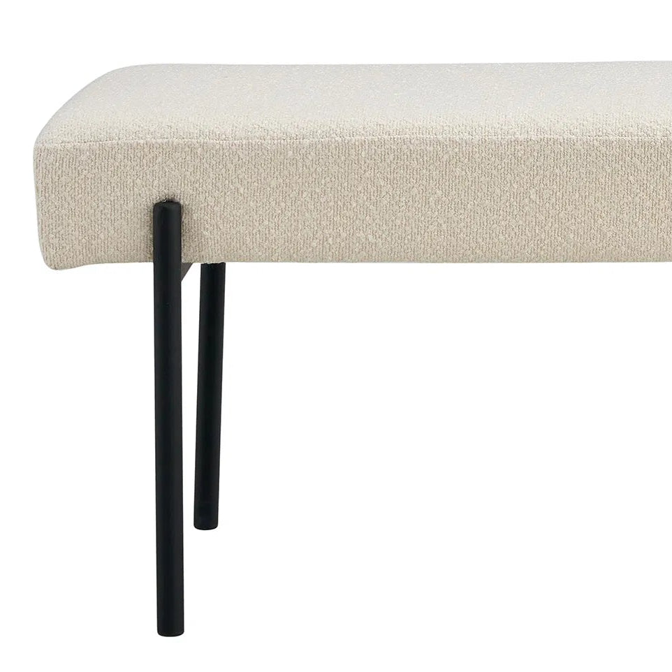 Polstret benk med svart ramme og kremfarget boucléstoff ved siden av dekorativ plantekrukke.