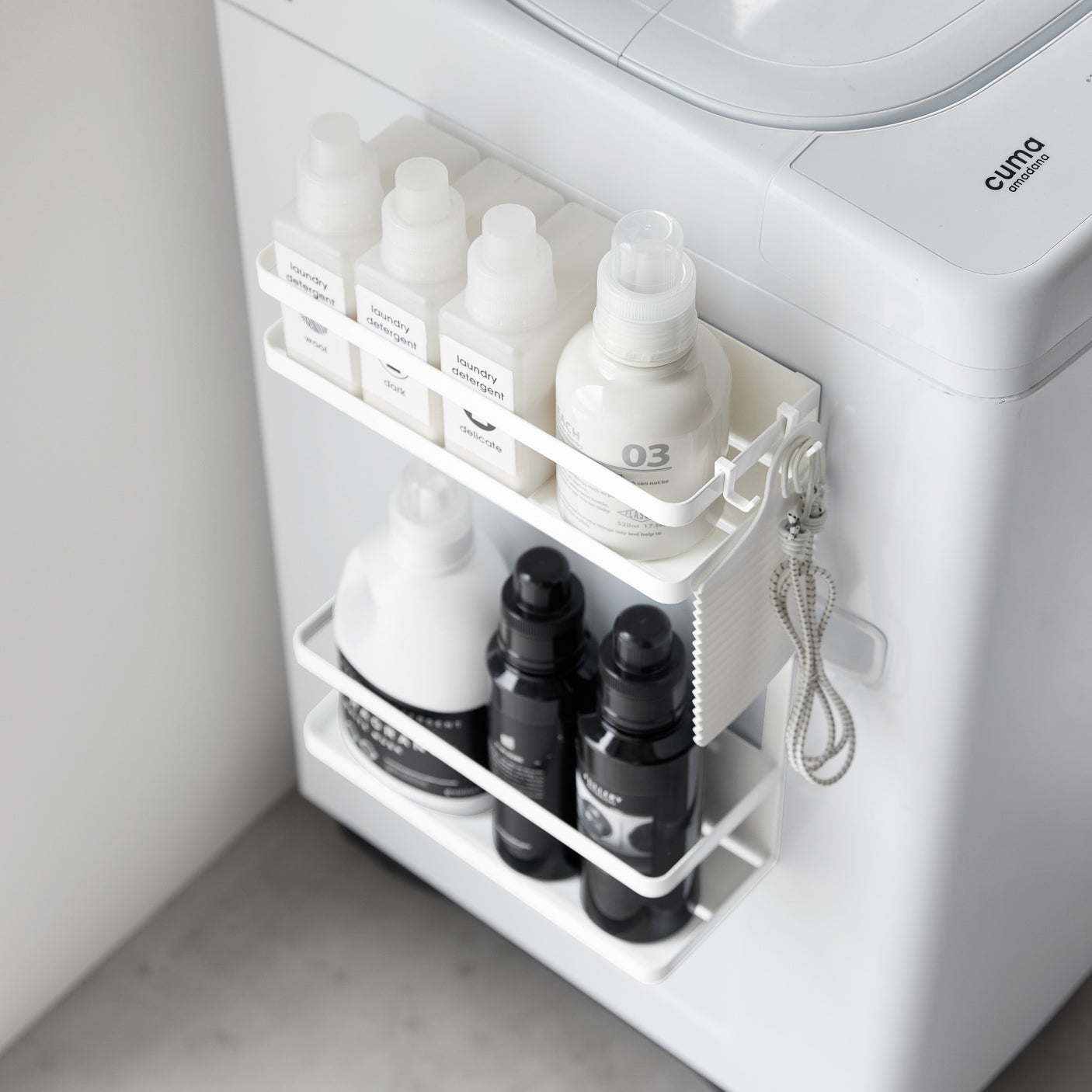 Hvit metallhylle festet uten skruer på vaskemaskin med rengjøringsartikler.