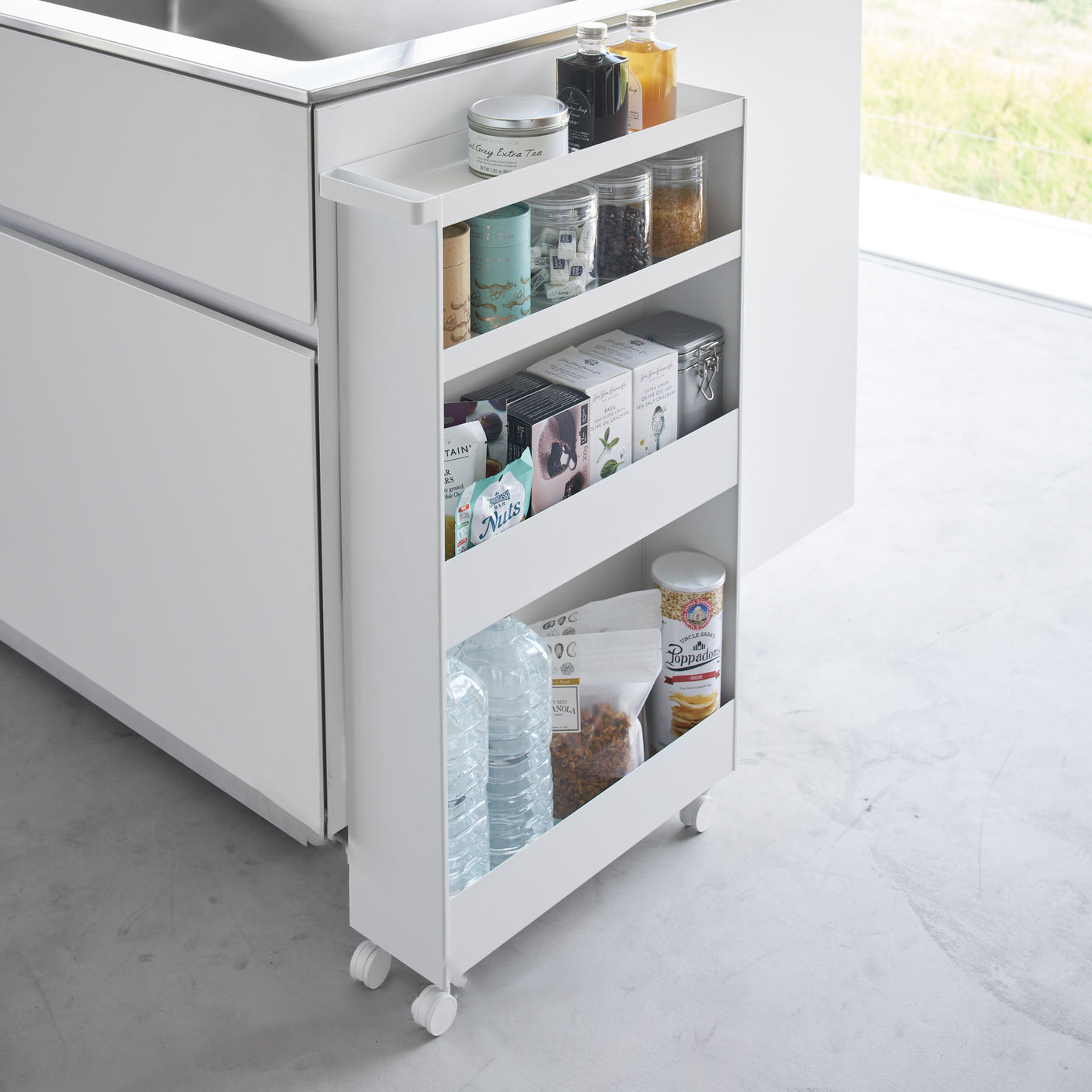 Hvit oppbevaringsvogn på hjul mellom vaskemaskin og skap.