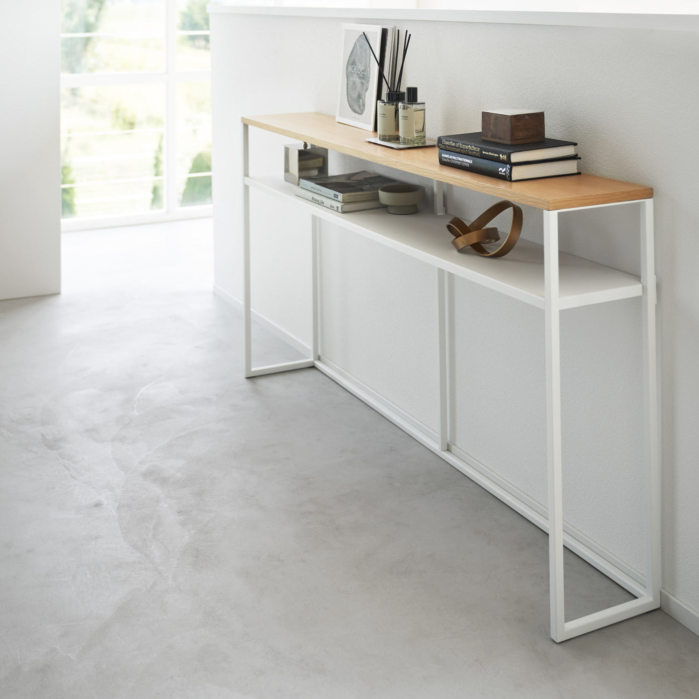 Hvit metallramme og trehylle på konsollbord ved vindu.