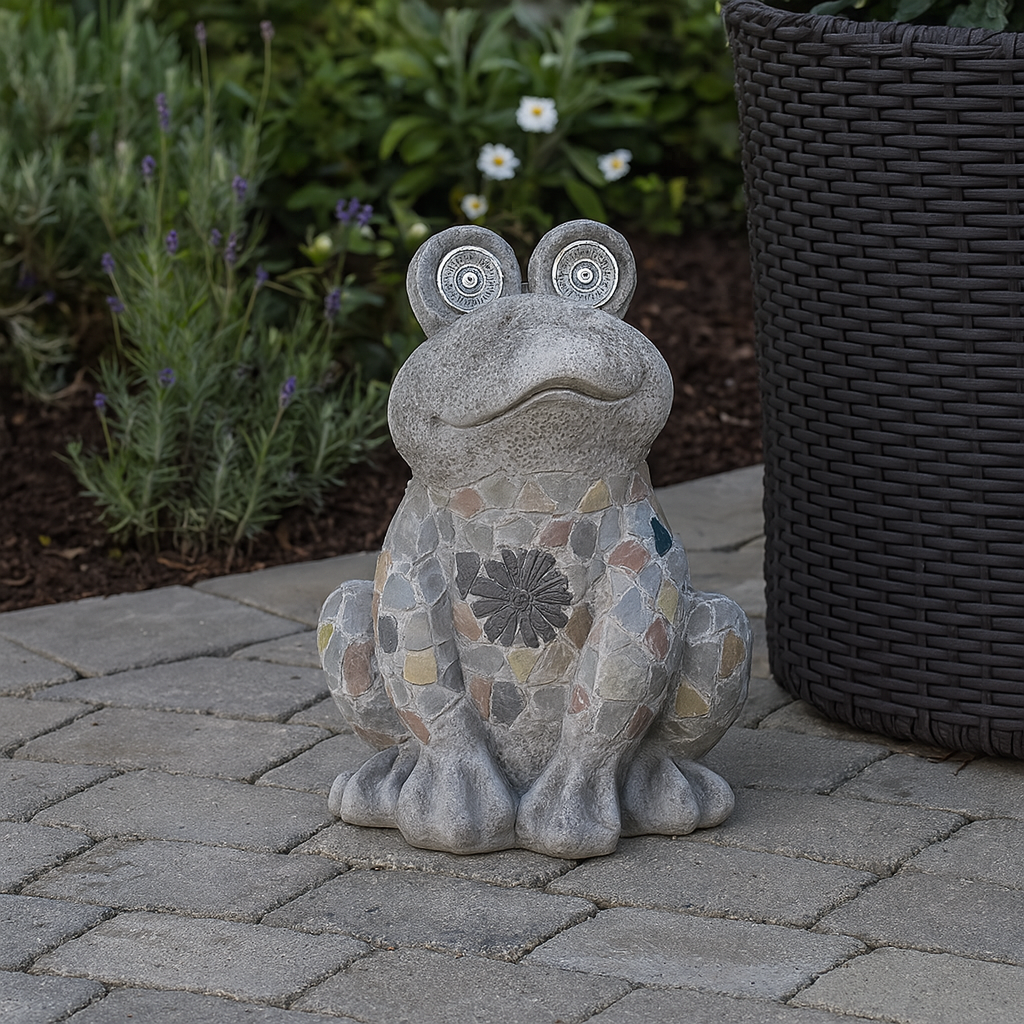 froskefigur står på steinbelagt uteplass i dagslys, omgitt av blomstrende planter og en flettet blomsterpotte.
