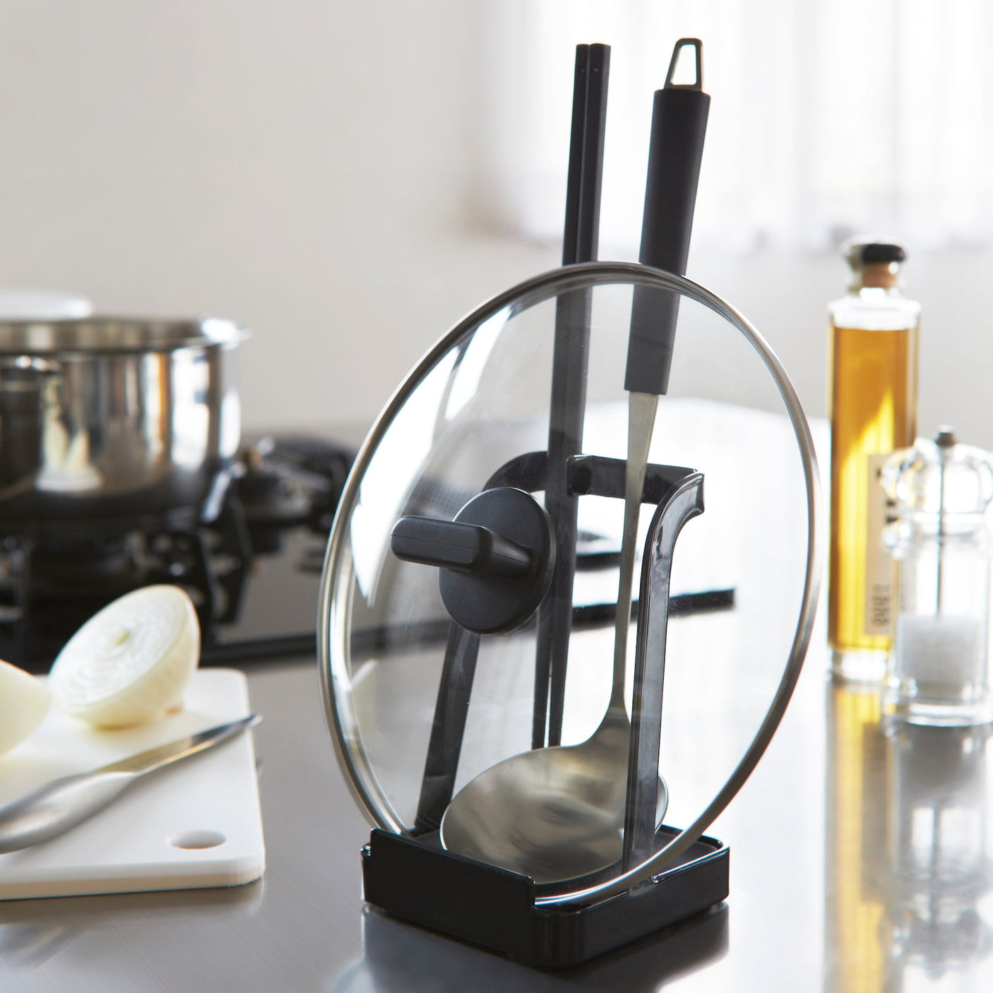Sort stativ for kjøkkenredskaper på kjøkkenbenk, brukt til sleiver, lokk og redskap under matlaging.