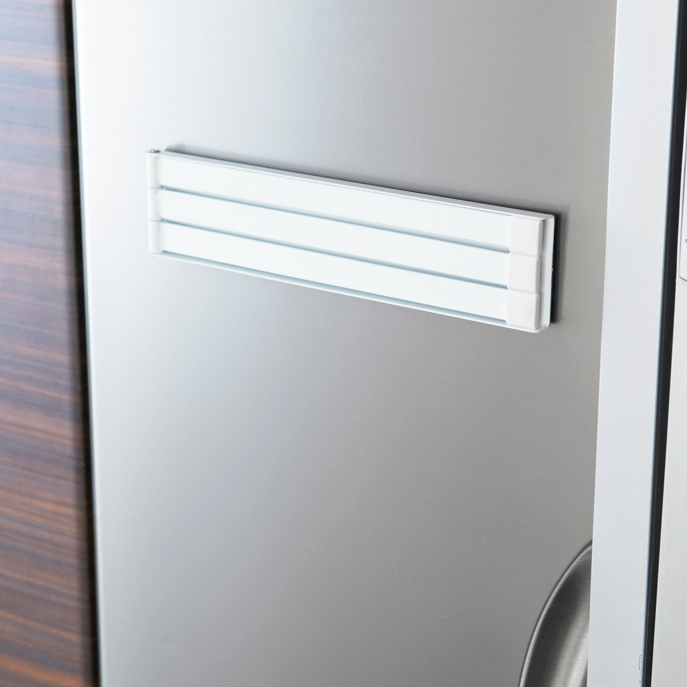 Nærbilde av håndkleholderen i hvit, festet på en metalloverflate.