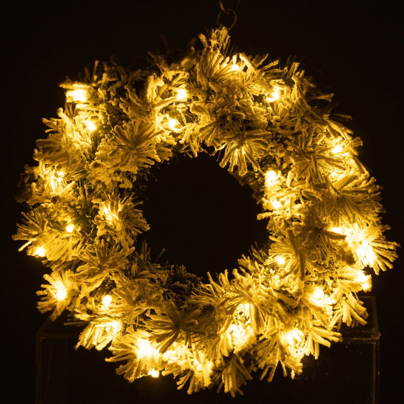 Lysende julekrans med snø i mørket, gir varm og stemningsfull glød.