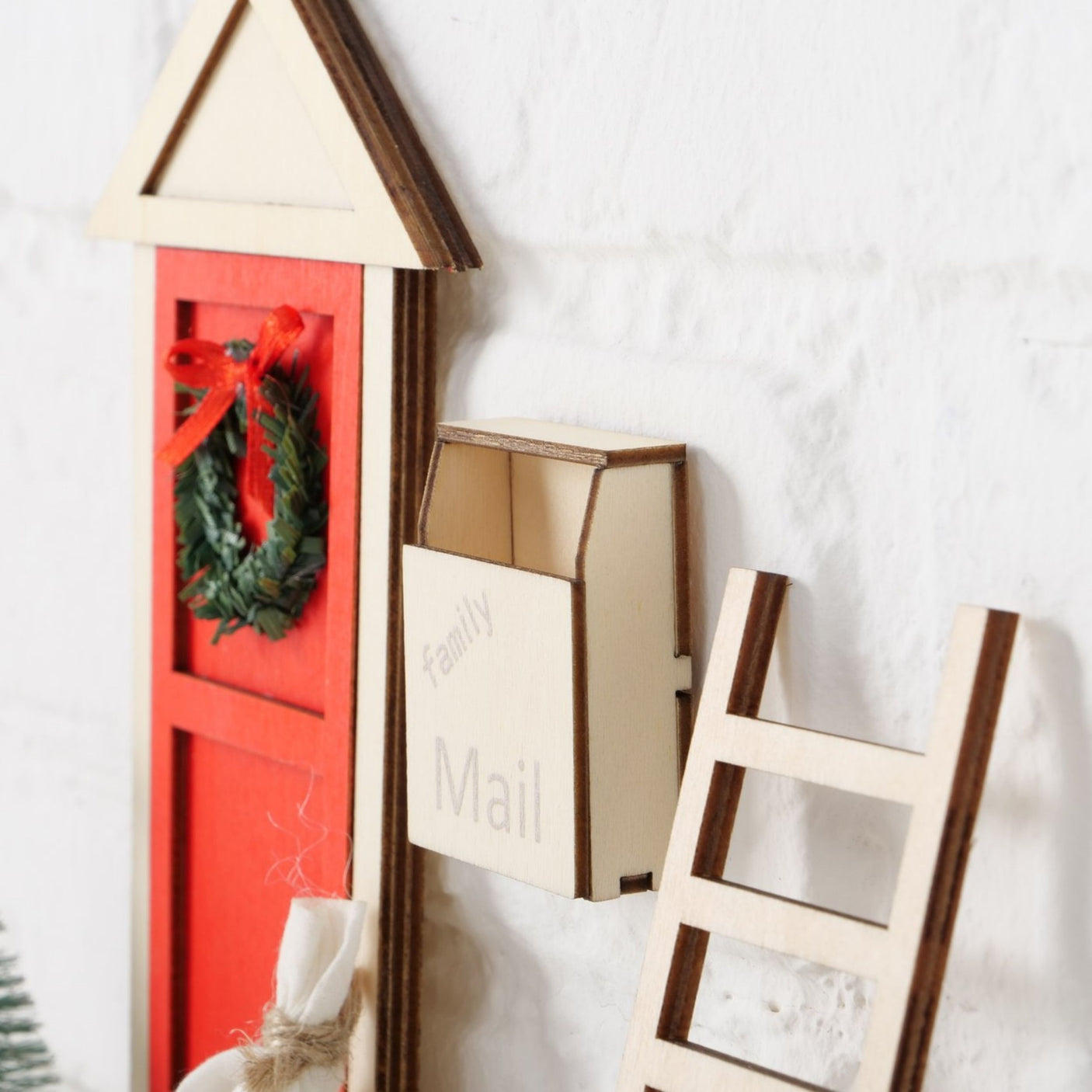 Rød miniatyrdør med julekrans, hvit postkasse og stige på vegg.