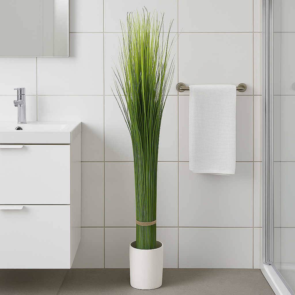 Høy kunstig gressplante i hvit potte plassert på et stilrent bad med servant og håndkleholder.