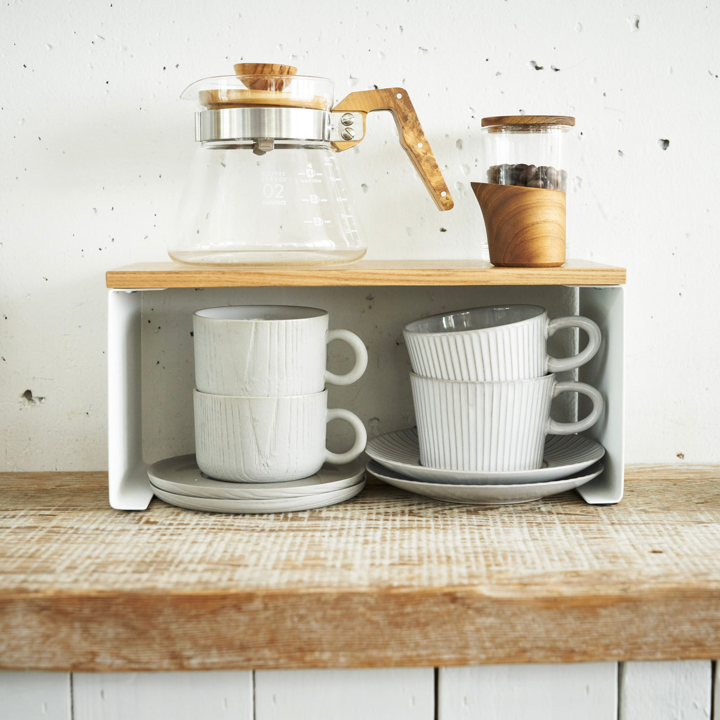 To stabelbare hyller i hvit farge med kopper og krydderglass på kjøkkenbenk.