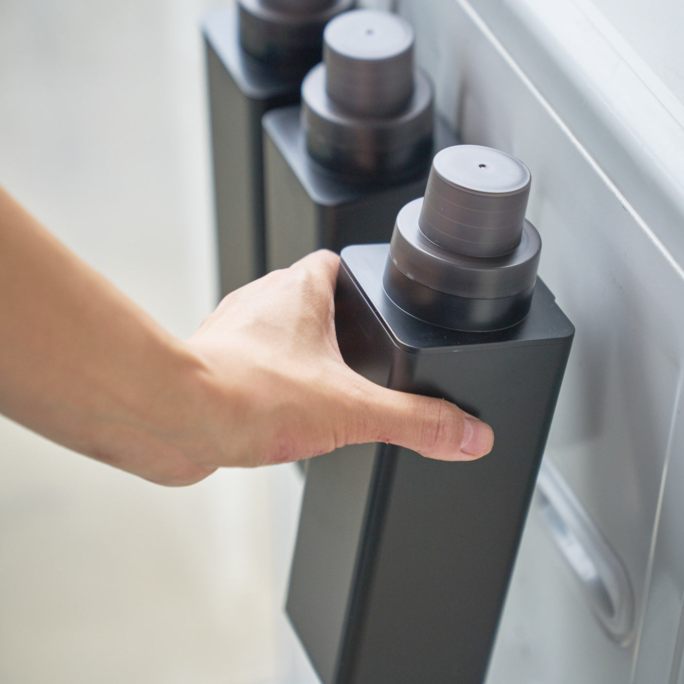 Sort magnetisk flaske for oppvaskmiddel festet på vaskemaskin.