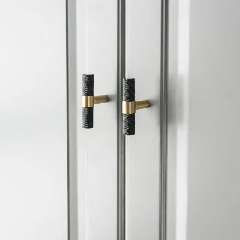 To sorte og messingfargede T-bar håndtak montert på grå skapdører.