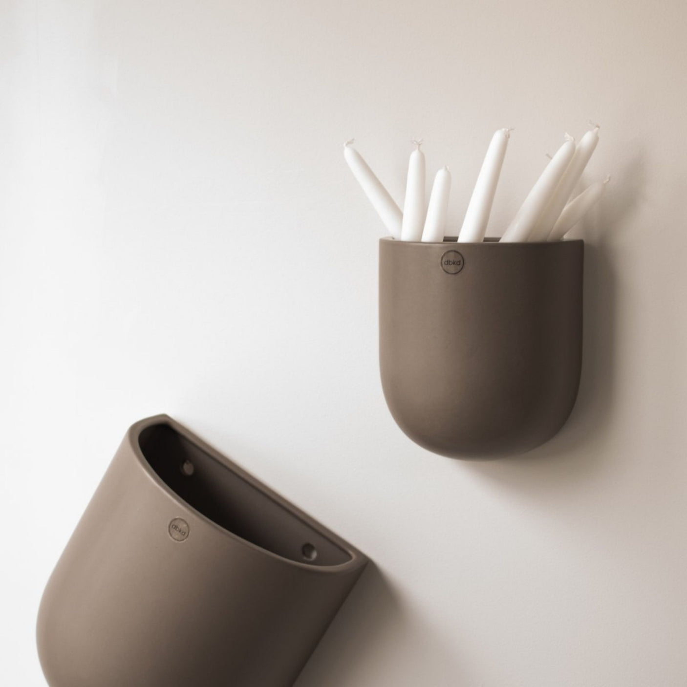 To keramikkpotter henger på hvit vegg, én fylt med hvite kronelys.