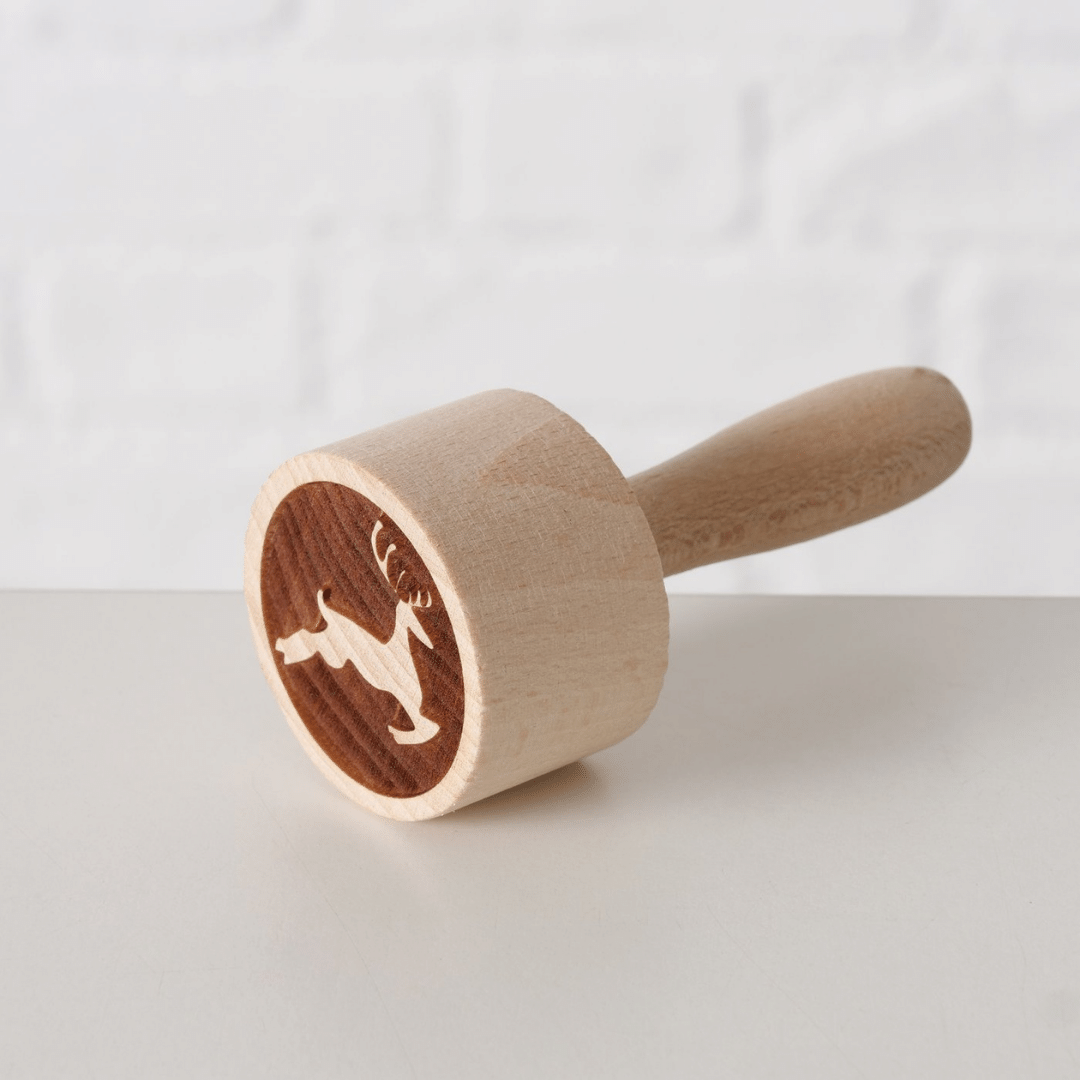 Kakestempel i tre med hoppende reinsdyrmotiv, liggende på lys overflate.