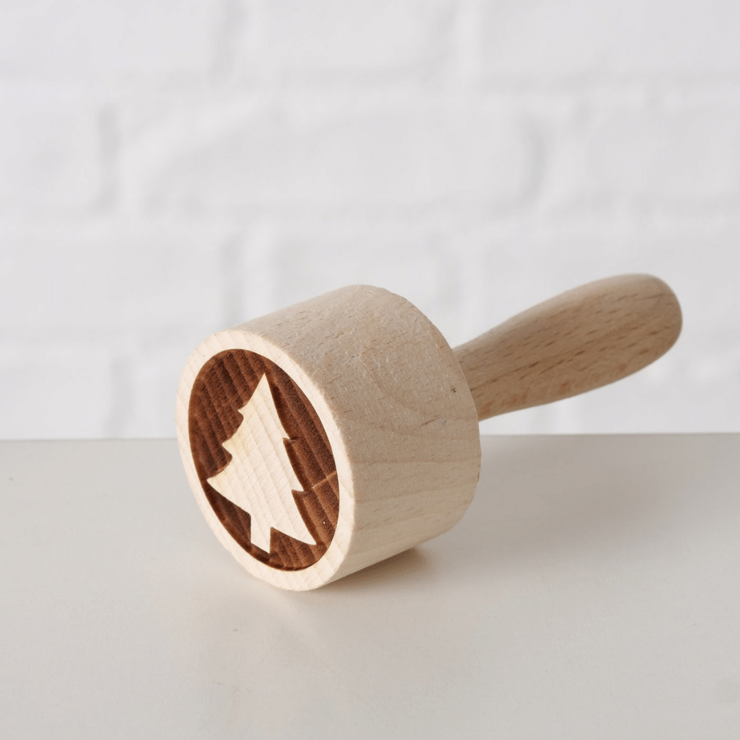 Kakestempel i tre med juletremotiv, liggende på lys overflate.