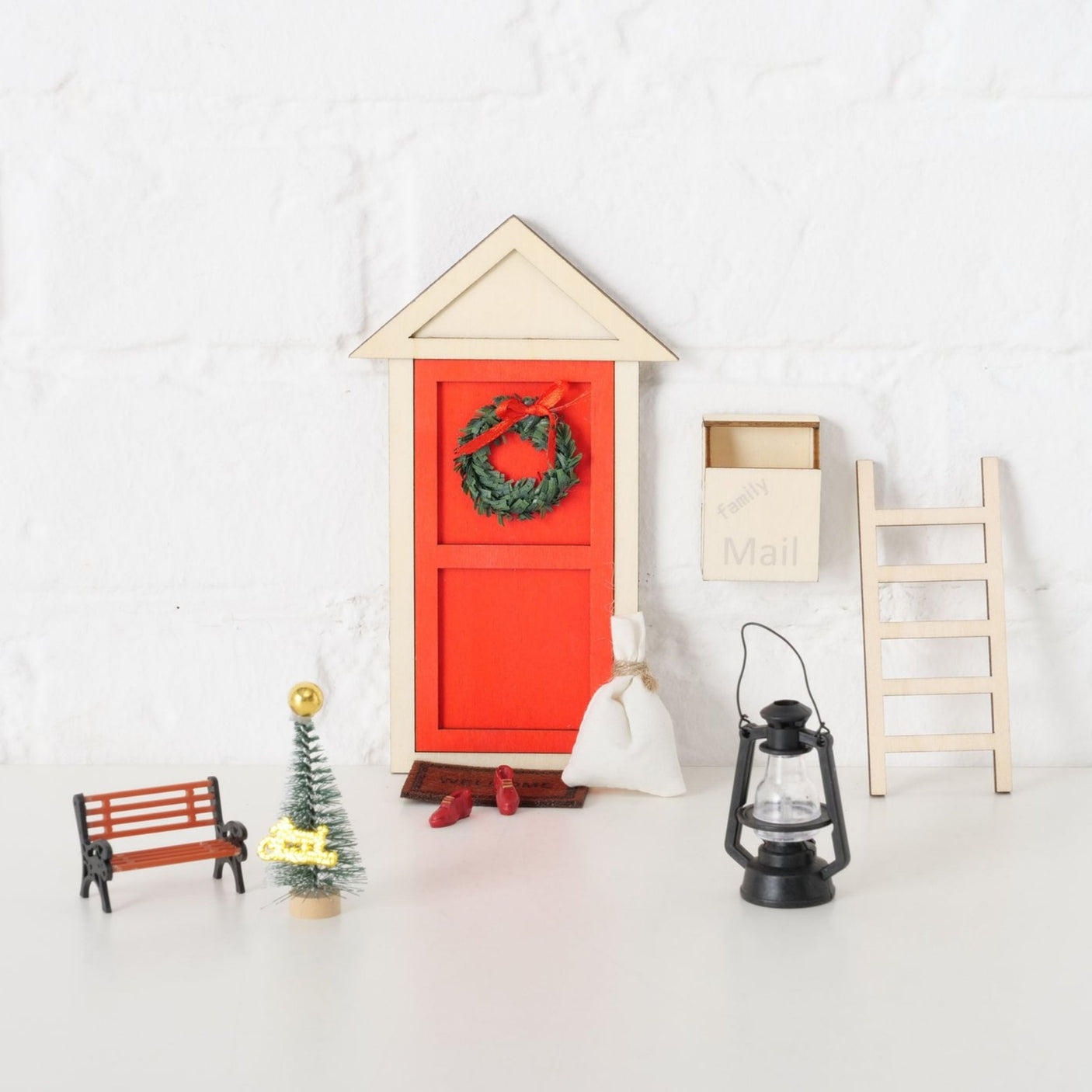 Liten juletrepynt, velkomstmatte, røde sko og sekk foran rød miniatyrdør.