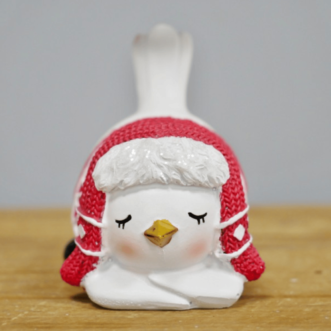 Hvit julefugl med røde ørevarmere og vinterjakke, sittende.