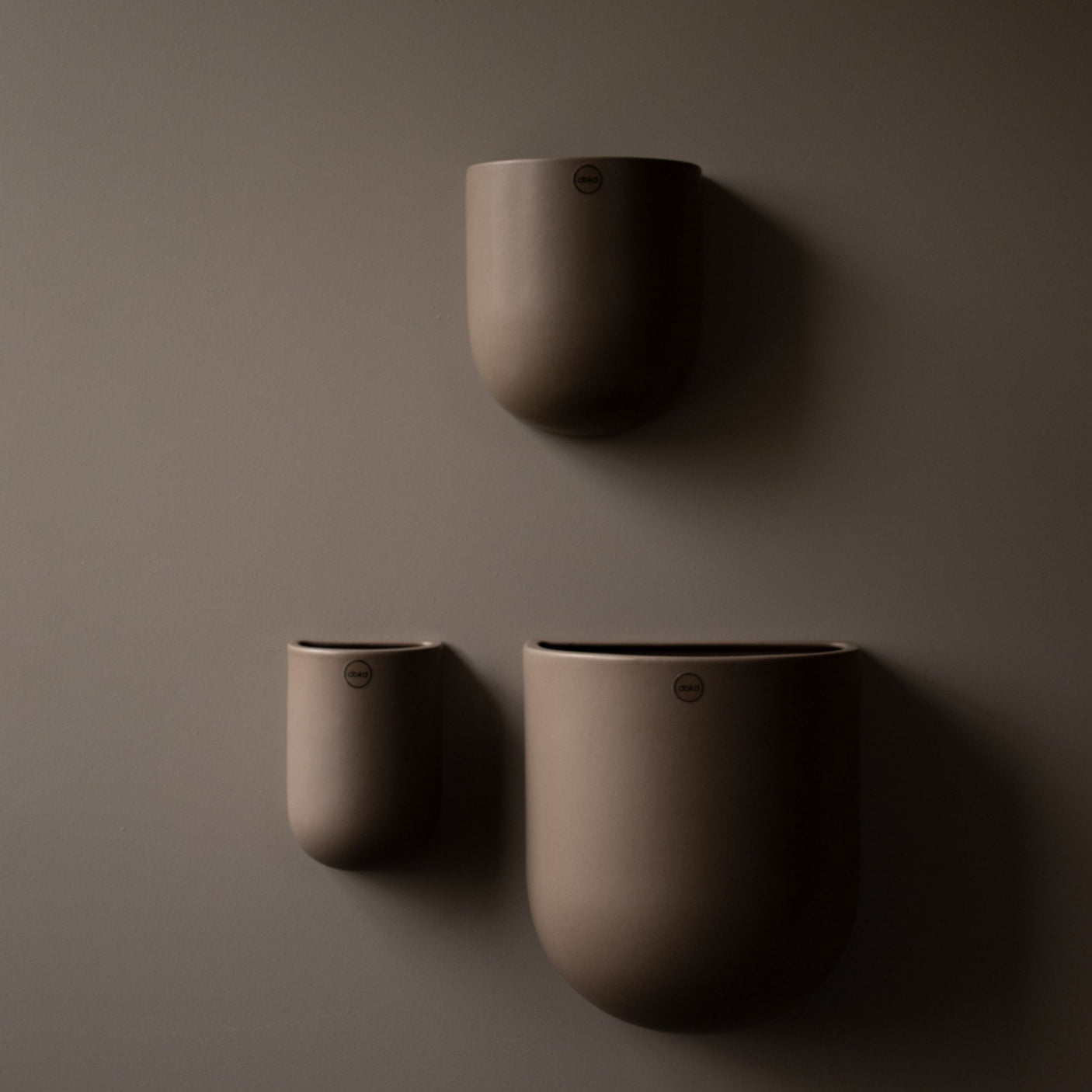 Tre keramikkpotter fra dbkd montert på mørk vegg i ulike størrelser.