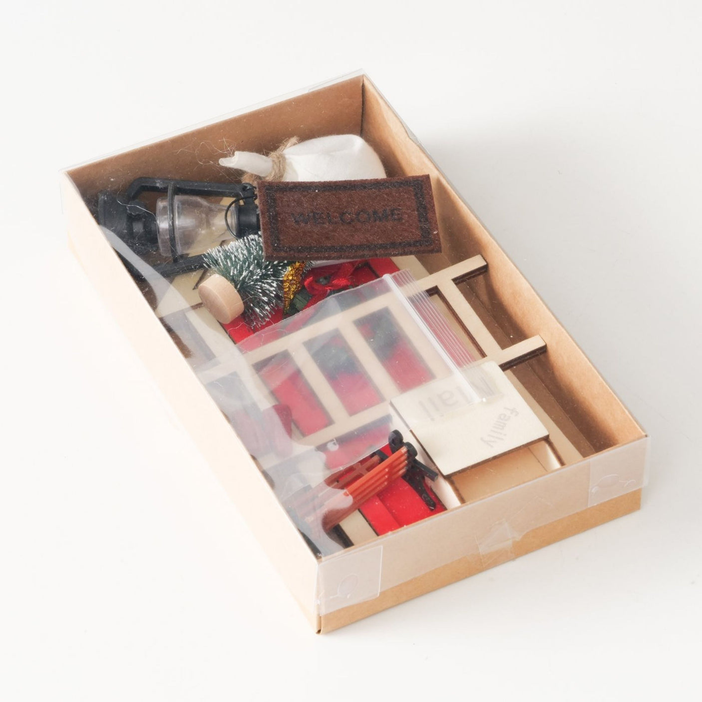 Miniatyrsett i eske med rød dør, julekrans, stige, lykt, benk, juletre, velkomstmatte og små røde sko.
