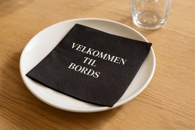 Fotorealistisk serviett med teksten Velkommen til bords, plassert lett brettet på tallerken i lys borddekking med naturlig dagslys. Perfekt dekorasjon til konfirmasjon, dåp, bryllup eller fest.