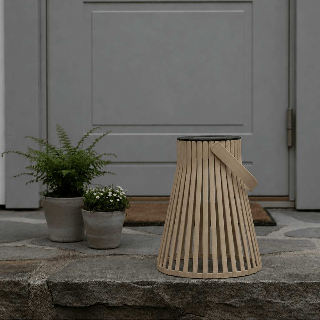 Brun solarlykt plassert ved et inngangsparti med grå dør, steinhelle og grønne planter i potter. - Lindas dekor