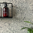 "London terrazzo selvklebende fliser på baderomsvegg med såpeflaske og svart metallhylle"