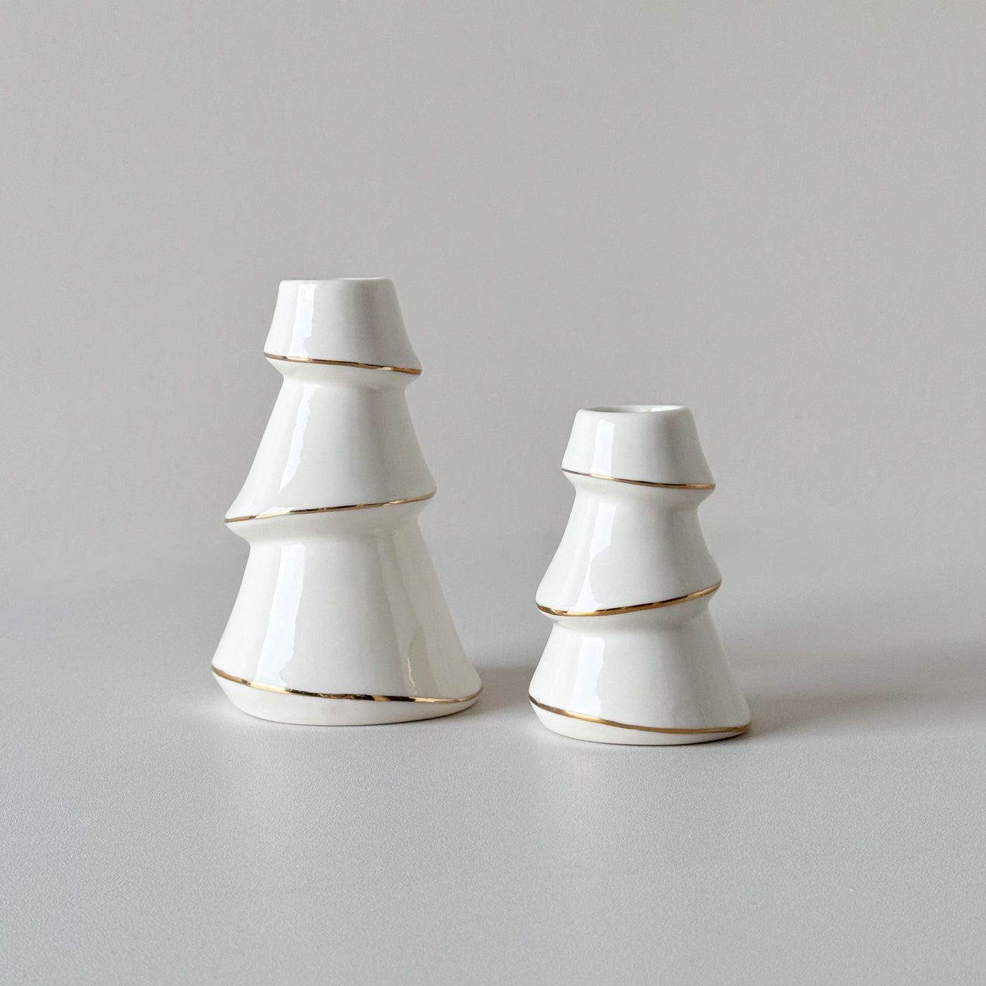 To hvite lysestaker formet som juletrær i ulik størrelse med gullkant.