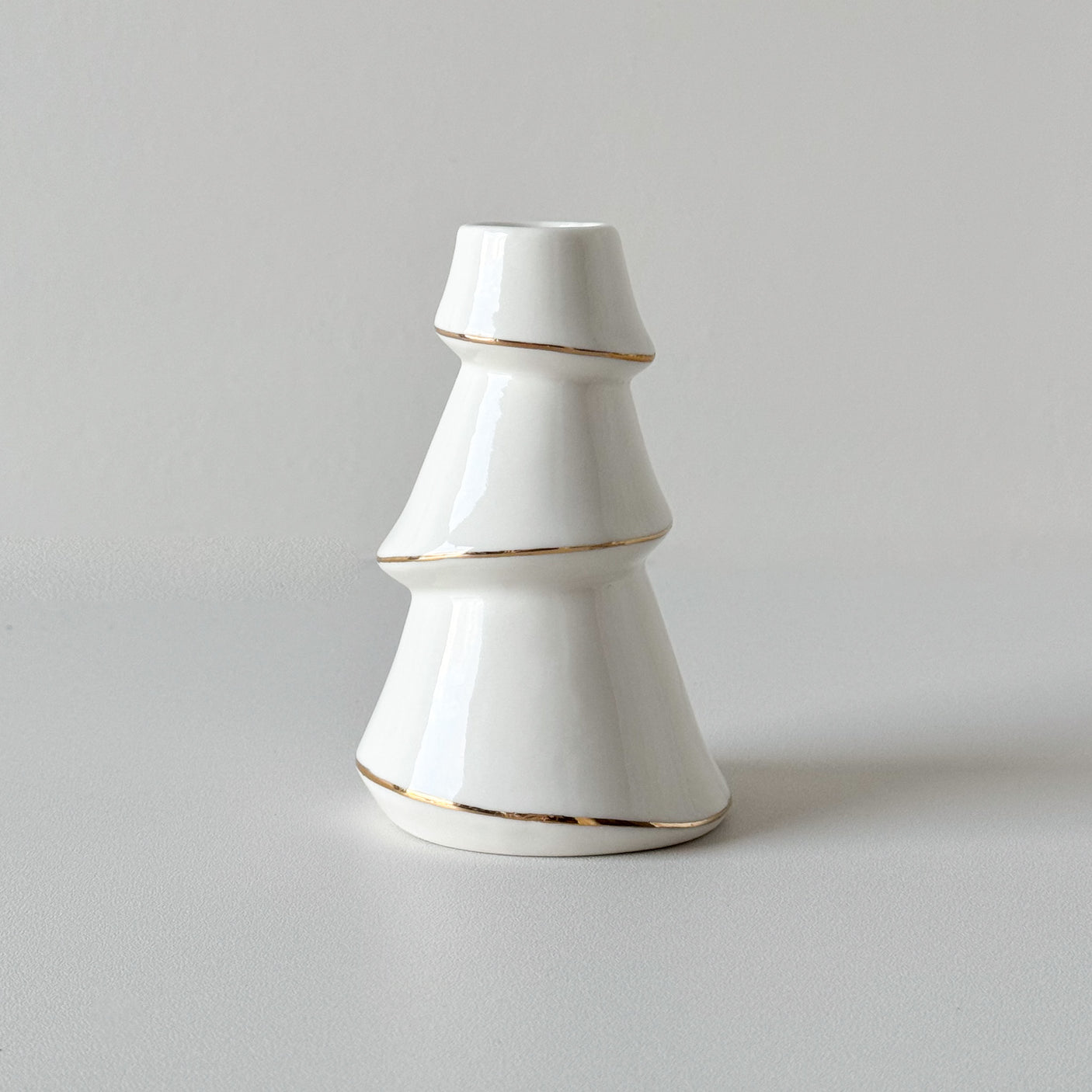 Hvit lysestake formet som juletre med gullkant, vist mot lys bakgrunn.