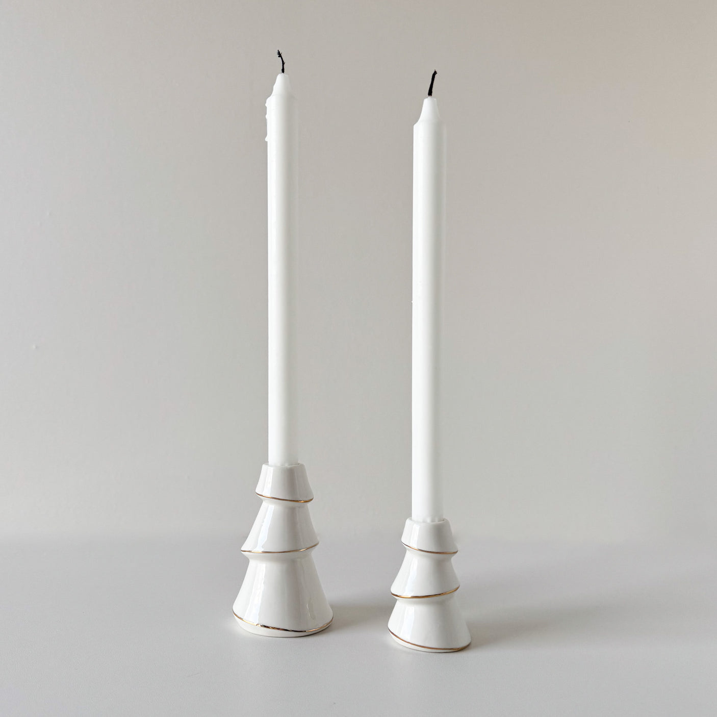 To hvite lysestaker formet som juletrær med høye hvite stearinlys.