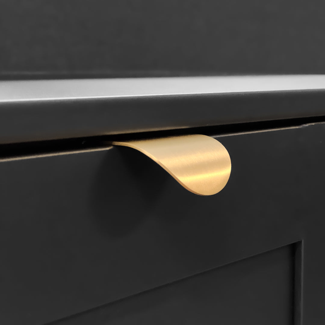 Roma håndtak i messing montert på svart skuffefront i moderne interiør.