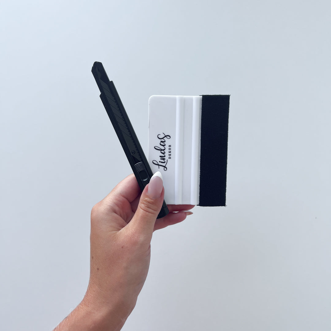 Hånd holder tapetkniv og foliesletter fra Lindas Dekor, perfekt til montering av folie.