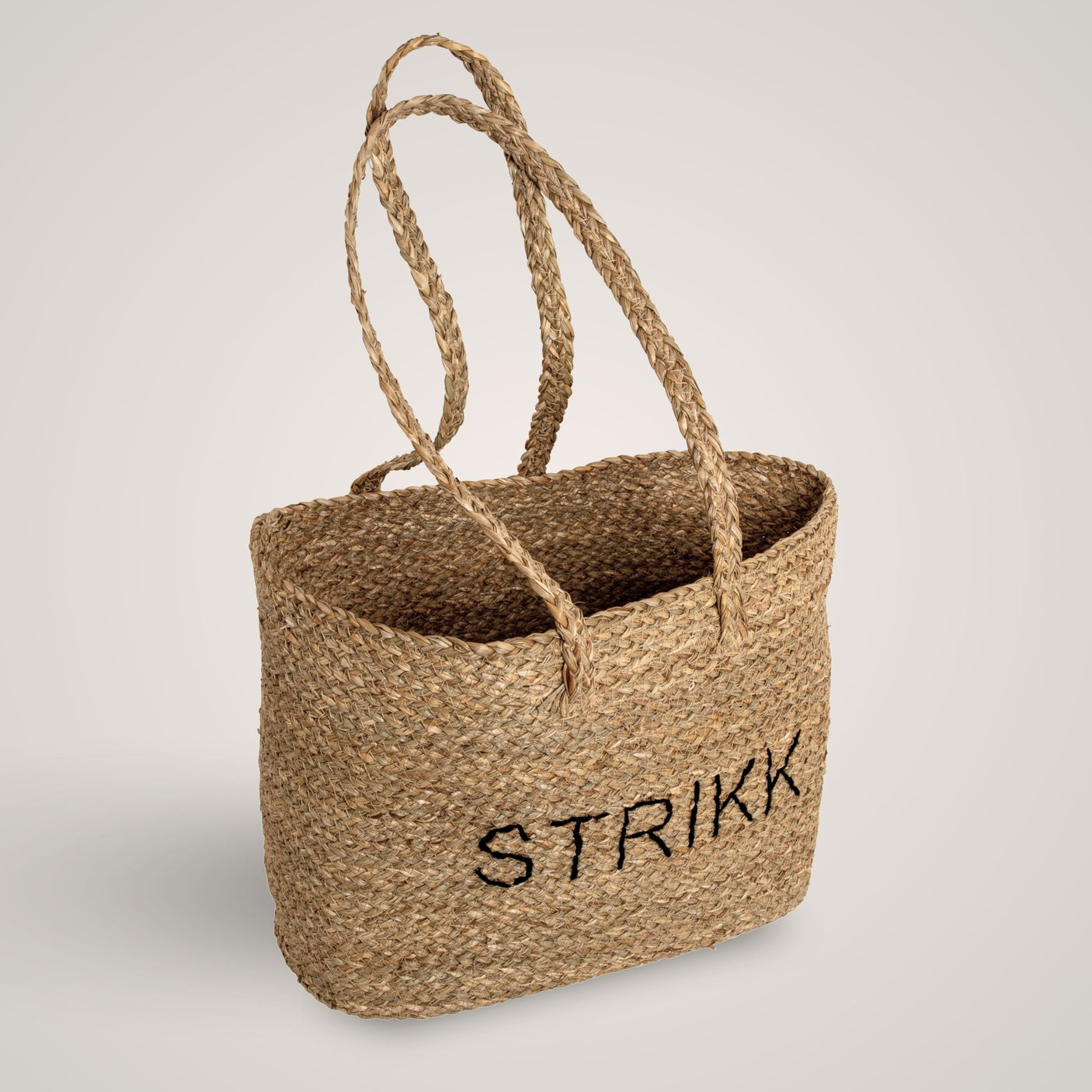 Håndlaget stråveske med teksten STRIKK, to flettede hanker og naturlig tekstur. Perfekt til hobby og oppbevaring.