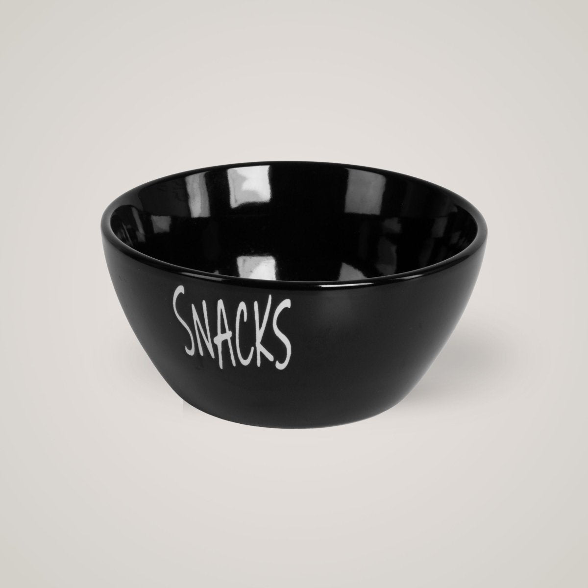Sort snacks-skål med hvit tekst, plassert mot lys beige bakgrunn.
