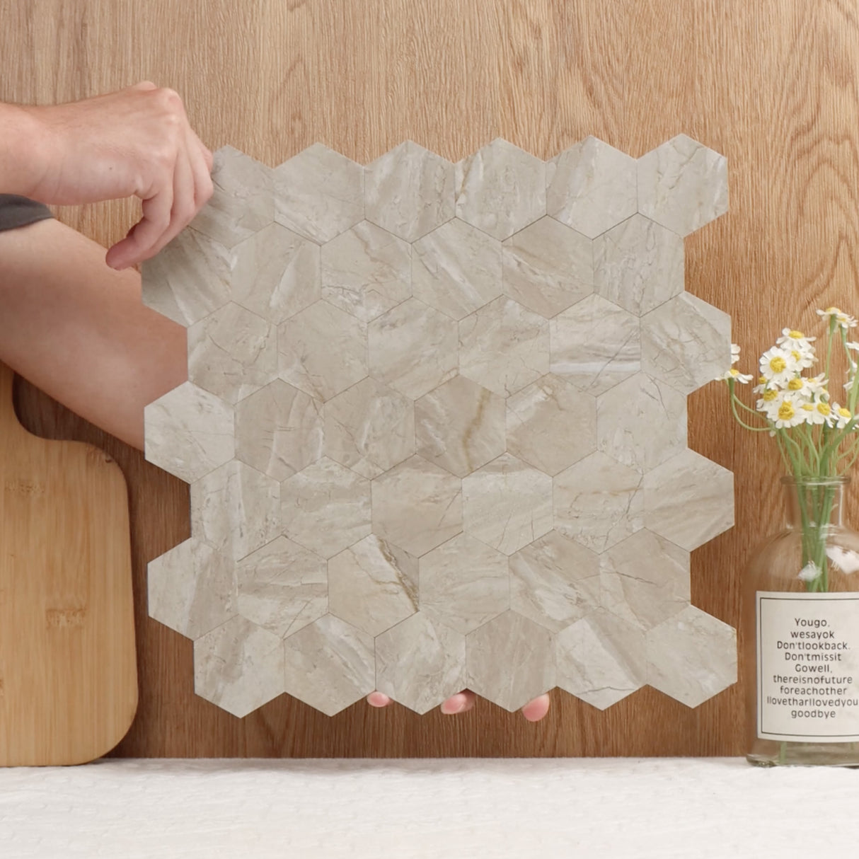Grace hexagon selvklebende fliser i beige marmor-look holdt i hånden, viser fleksibel og lett design for enkel montering på kjøkkenvegger eller baderomsvegger.