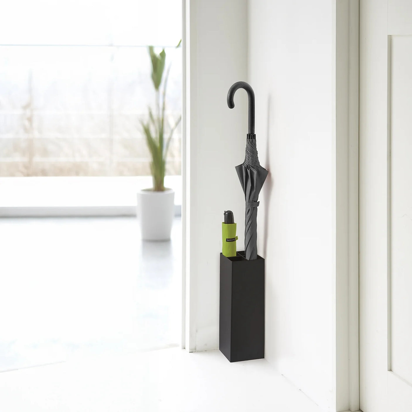 Sort paraplyholder i stål plassert i hjørne ved inngangsparti