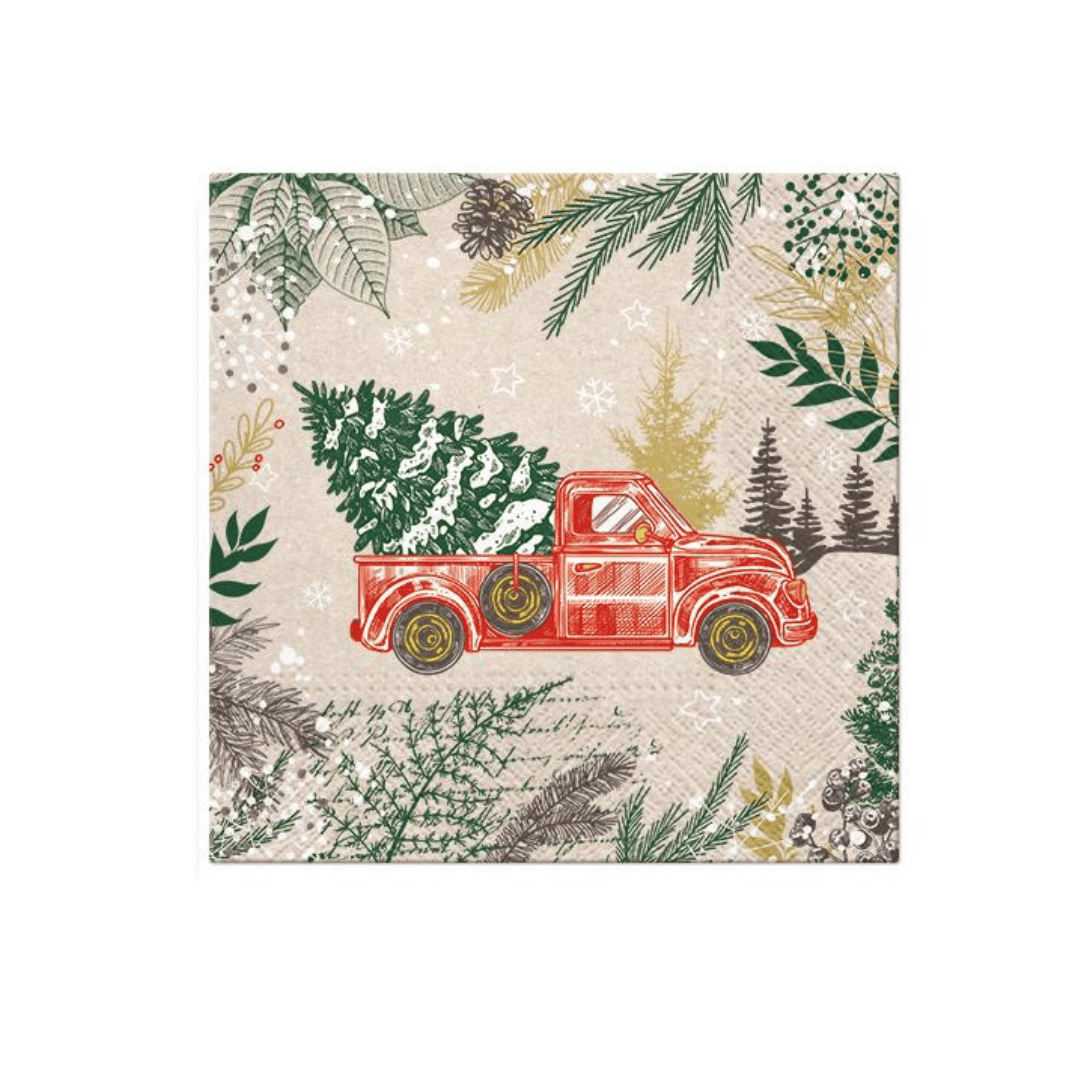 Juleserviett med motiv av rød lastebil som frakter juletre, plassert på et bord omgitt av granbar, gaver og tente lys foran et juletre.