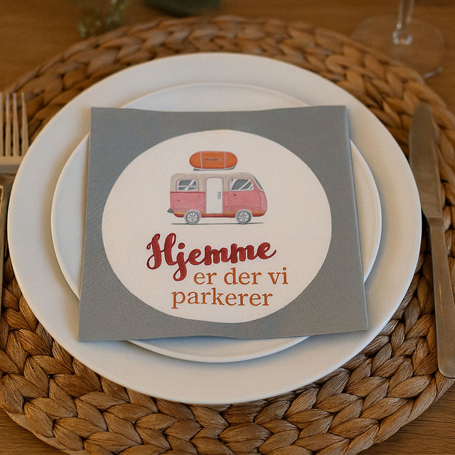 Serviett med campingmotiv og teksten «Hjemme er der vi parkerer» – perfekt til borddekking i bobil, campingvogn eller sommermiddag.