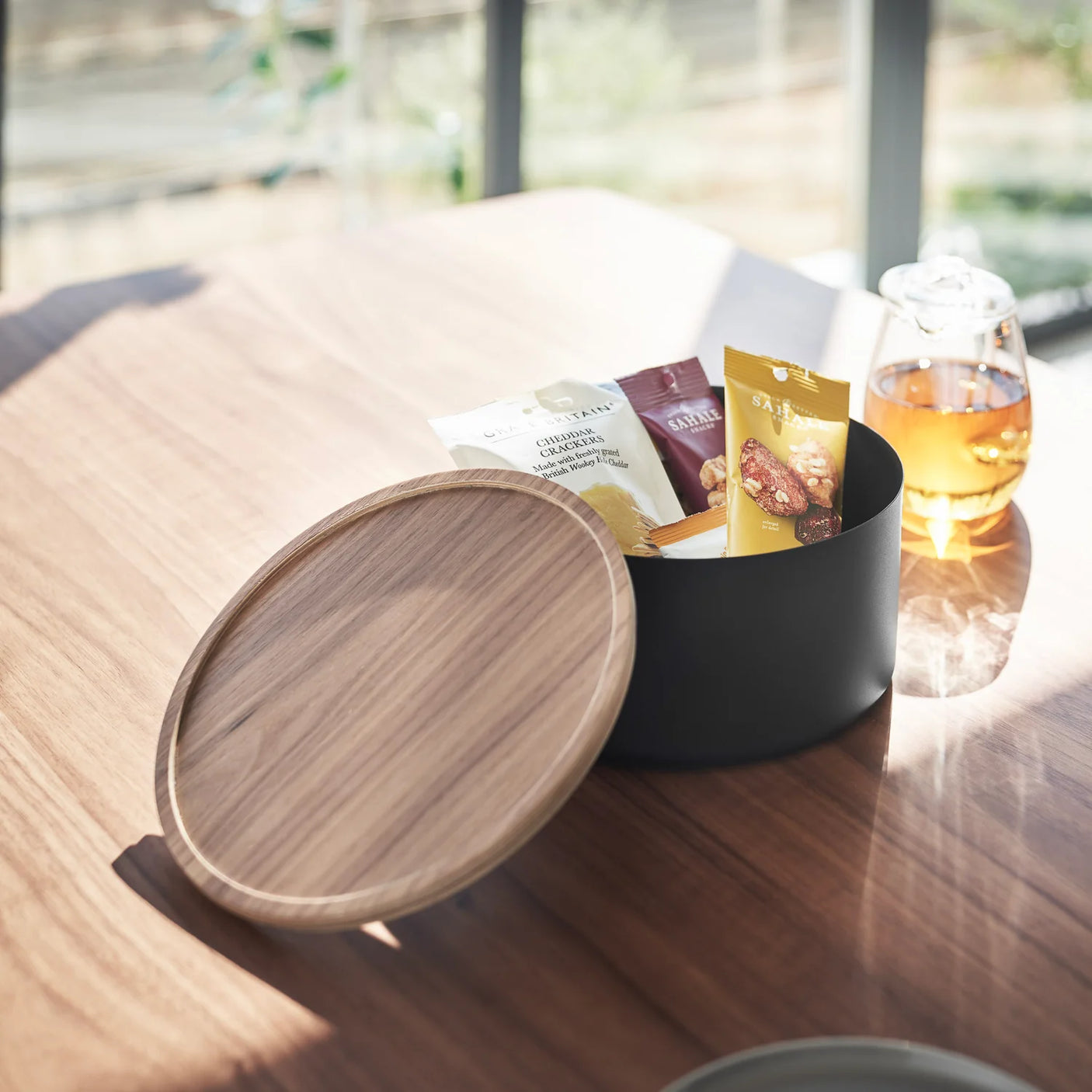 Dyp rund oppbevaringsboks i sort stål med trelokk på lys bakgrunn