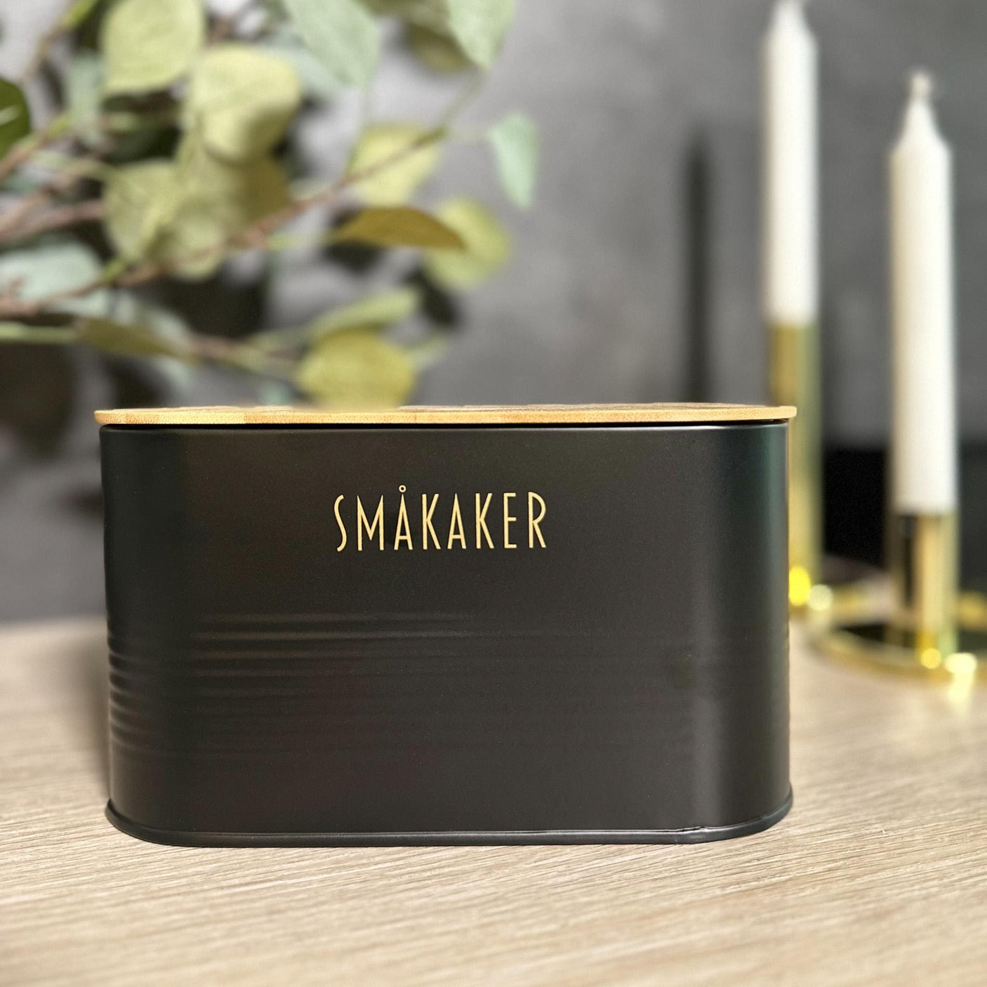 Sort metallboks til småkaker med naturlig bambuslokk, i moderne kjøkkeninteriør.