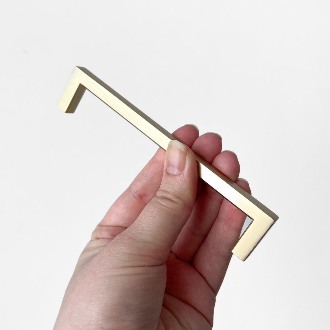 Hånd holdt håndtak i børstet messing med moderne, minimalistisk design.