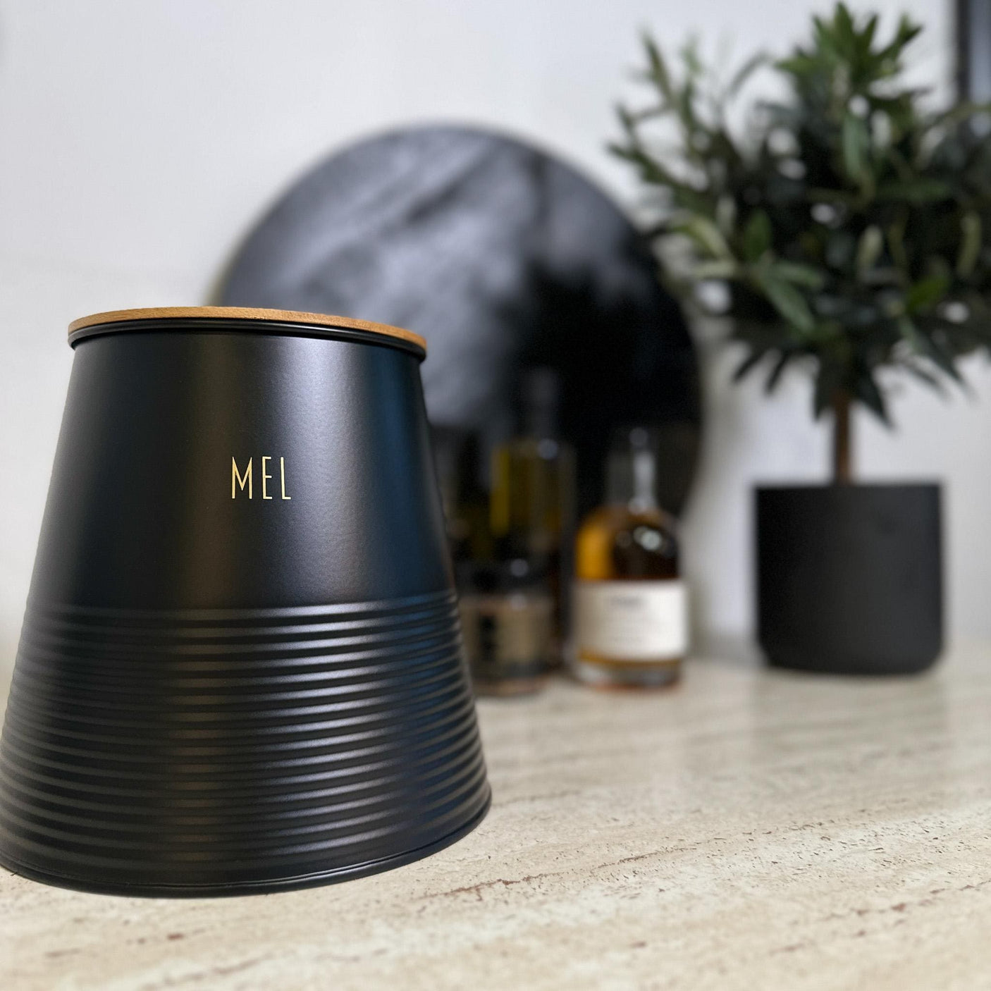 Sort boks med teksten «Mel», bambuslokk og skje – stående på kjøkkenbenk.