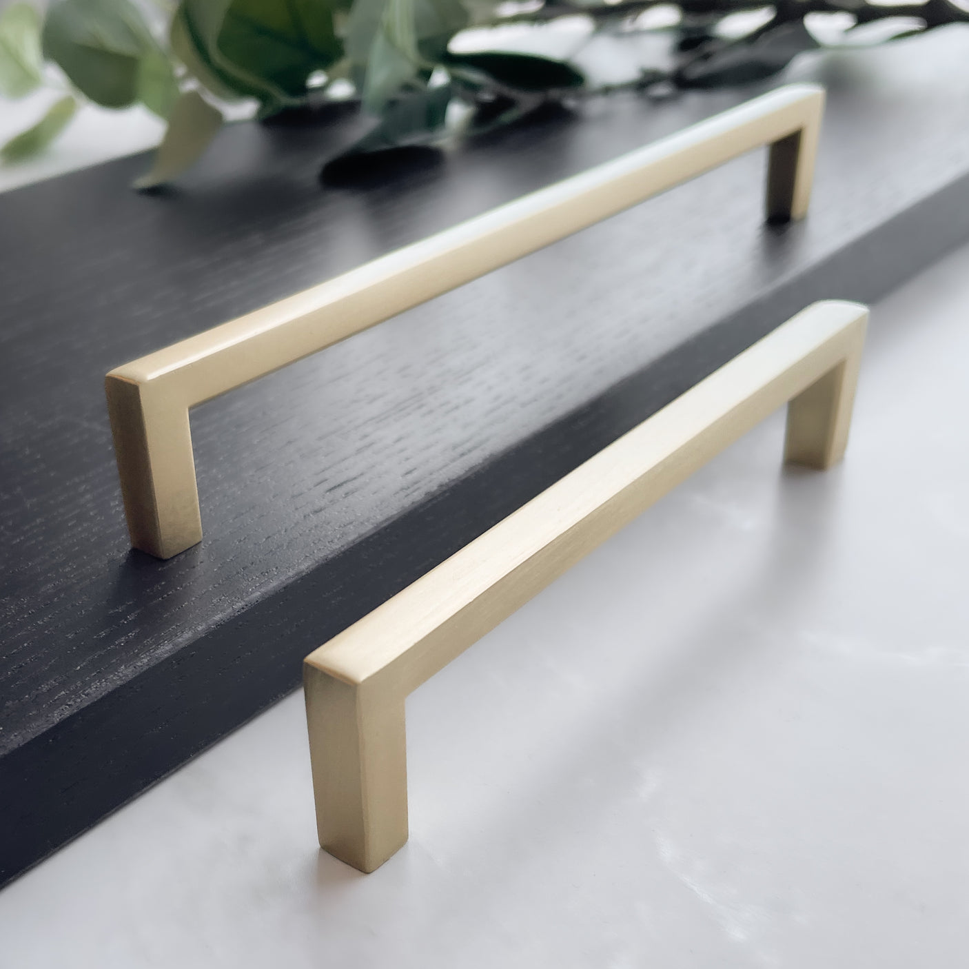 Stilrent møbelhåndtak i metall holdt i hånd mot hvit bakgrunn.