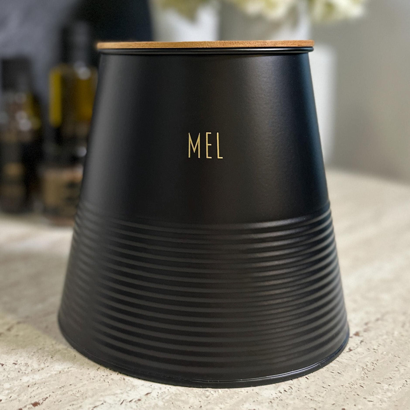 Sort metallboks til mel med bambuslokk og gulltekst «Mel» på kjøkkenbenk.