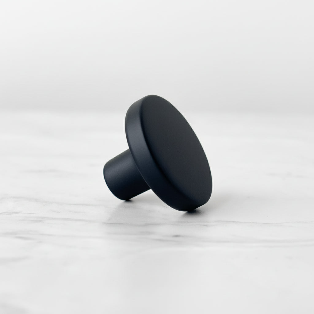 Sort matt knott med rund form og glatt overflate, fotografert liggende på en lys marmorinspirert bakgrunn.