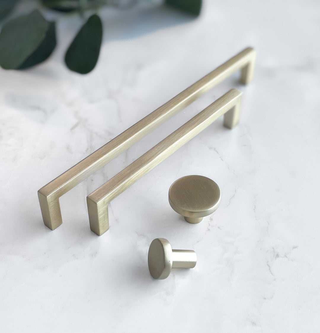 Stilrent møbelhåndtak i metall holdt i hånd mot hvit bakgrunn.