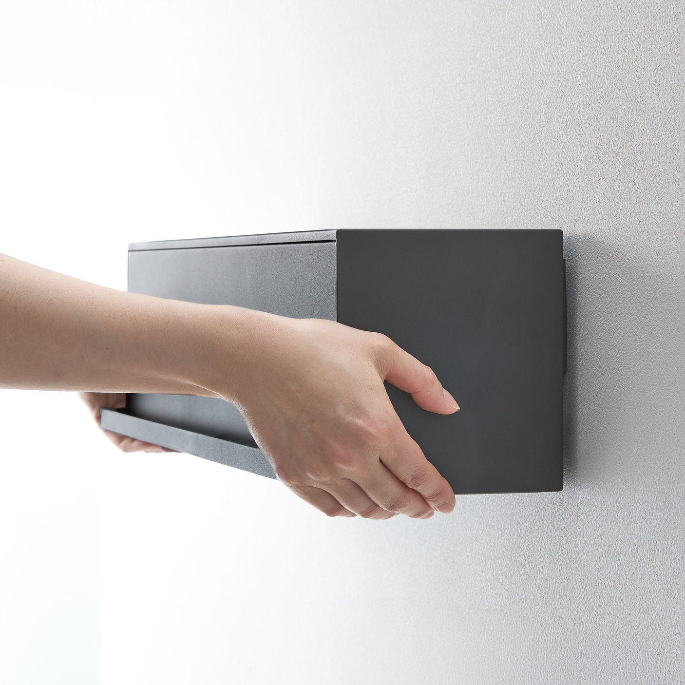 Person åpner sort veggboks for å legge inn småting.