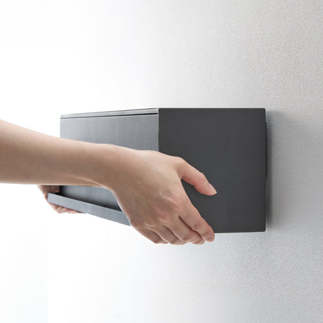 Person åpner sort veggboks for å legge inn småting.