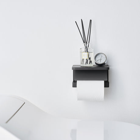 Elegant sort toalettpapirholder i metall, veggmontert modell med hylle til små baderomsartikler