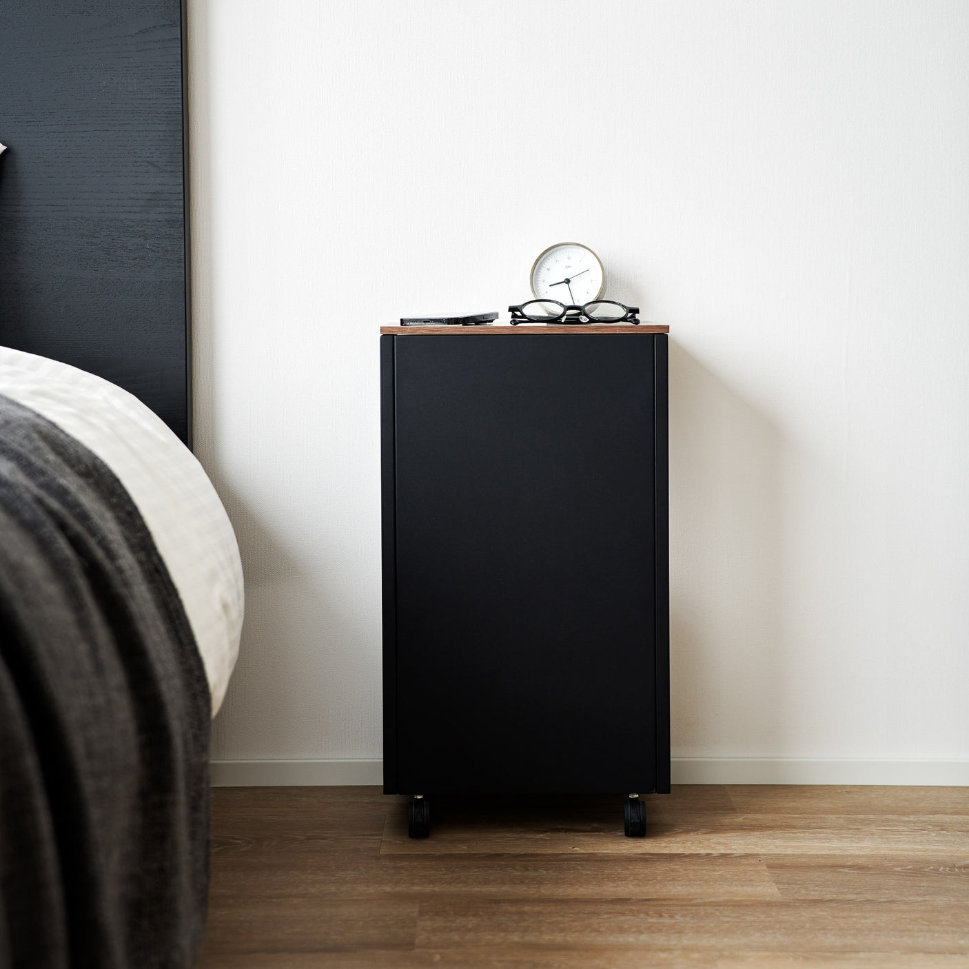 Sidebord i sort metall med bordplate i tre, plassert ved seng med lampe på toppen.