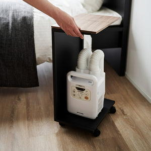 Praktisk sidebord i sort og tre, plassert ved seng med bøker og lampe.